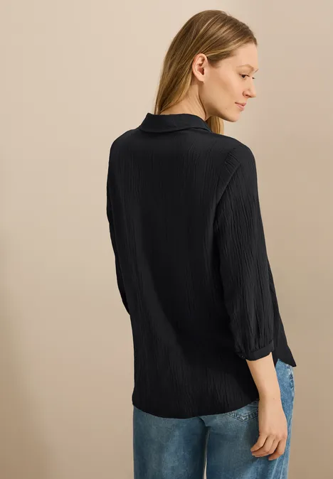 Frau mit schwarzen Hemd und Jeans steht seitlich, Blick nach unten.